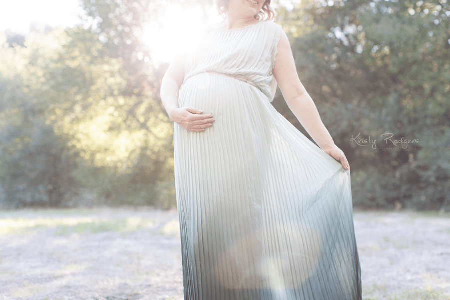 An expectant mother wearing a dress and holding her belly